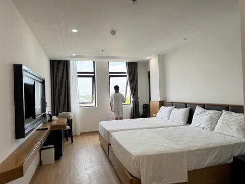 a hotel room with two beds and a man looking out the window at Sen Biển Hotel Luxury Sầm Sơn in Sầm Sơn