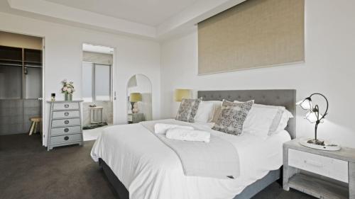 a white bedroom with a large bed and a dresser at The Coral Esplanade in Mornington