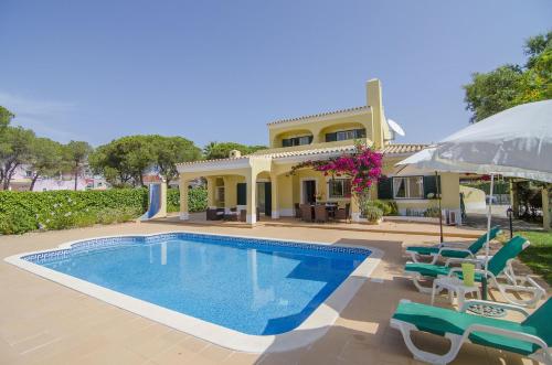 a house with a swimming pool and chairs and an umbrella at Bonita by Algarve Holidays in Quarteira