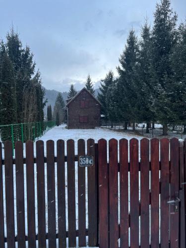 a wooden fence with a house in the snow at Mountain Cabin Retreat - Terrace, BBQ, Hot Tub in Lunca Bradului