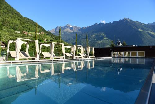 a pool with a row of white chairs next to a mountain at Giardino Marling in Merano