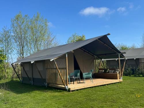 a tent with chairs and a deck in the grass at Camping de Boerenzwaluw in Zijdewind