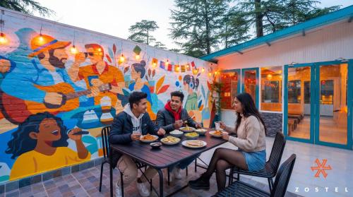 a group of people sitting at a table in front of a mural at Zostel McLeodganj in McLeod Ganj