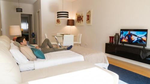 a man sitting on a white couch watching tv at Oriente Rio Apartments by APT IIN - Parque das Nações in Lisbon