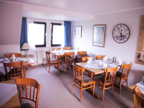 エッセンにあるHotel Zur Floraのテーブルと椅子、壁掛け時計のあるレストラン
