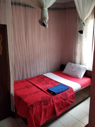 a bed with a red and white blanket and a window at Chumber Hotel in Gatunga