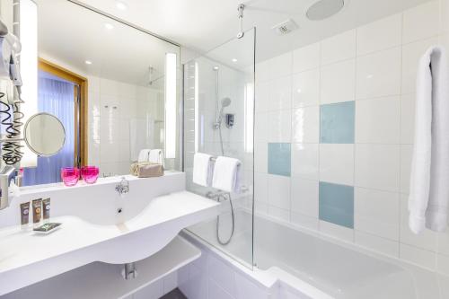 a white bathroom with a sink and a shower at Novotel München Airport in Freising