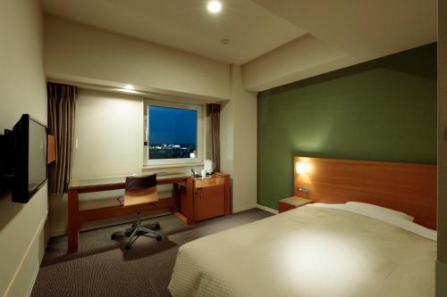 a bedroom with a bed and a desk and a window at Candeo Hotels Handa in Handa