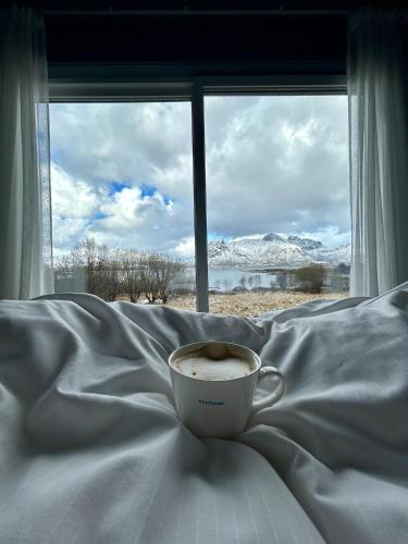 Eine Tasse Kaffee steht auf einem Bett vor einem Fenster. in der Unterkunft Oceanfront Cabin in Lyngedal