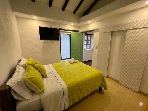 a bedroom with a bed with yellow sheets and a television at Hotel Bera-k in Villa de Leyva