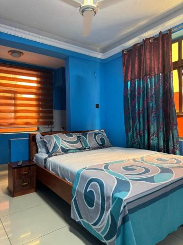 a bedroom with a bed with blue walls and a window at 247Hotel Apartments in Accra