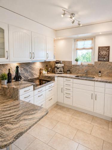 a kitchen with white cabinets and marble counter tops at Stylish house with garden, sauna & pool in Mörschwil