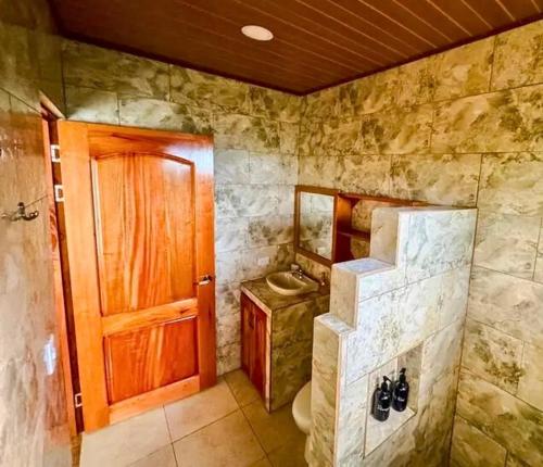 a bathroom with a toilet and a wooden door at Rio Celeste Birds Garden Apartments with air conditioning and Wifi Starlink in Upala