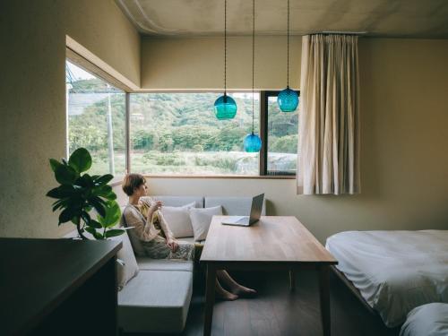 a woman sitting on a couch in a room with a window at semilla 名護 沖縄 in Nago