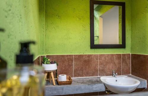 a green bathroom with a sink and a mirror at Six Pack Cottage in Chalong