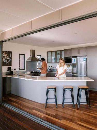 a woman standing at a kitchen counter with three stools at Wilderness House in Kulangoor