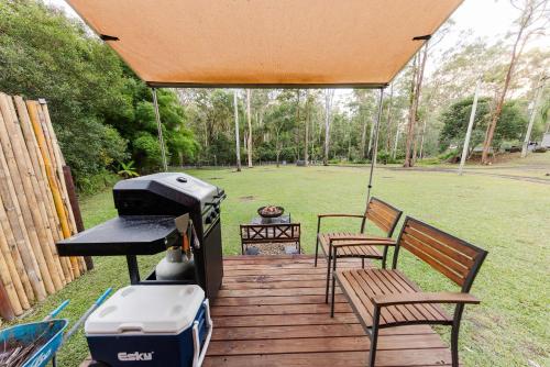 a grill and two chairs on a wooden deck at Cedar Creek Falls by Tiny Away in Mount Tamborine