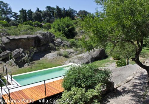 a swimming pool in a garden with trees and rocks at Cabañas Paititi in Villa Carlos Paz