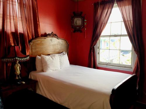 a bedroom with a white bed with red walls and a window at Creole Gardens Guesthouse and Inn in New Orleans