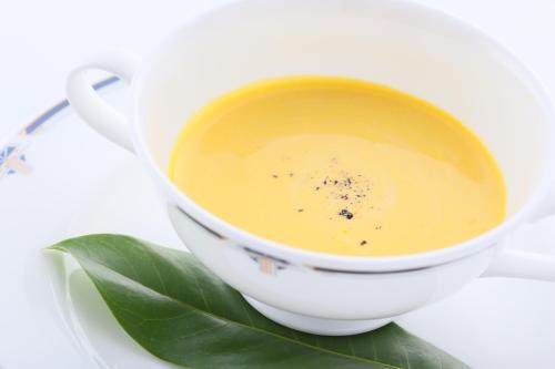 a cup of yellow soup with a green leaf on a plate at Kunugi Relaxation with 4 modern rooms in Hakuba