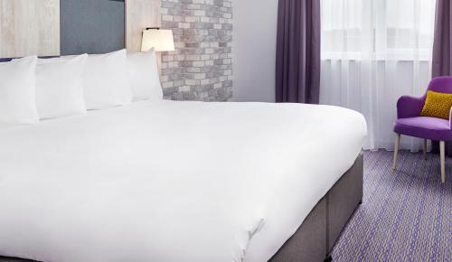 a large white bed in a room with a purple chair at Leonardo Hotel Swindon in Swindon