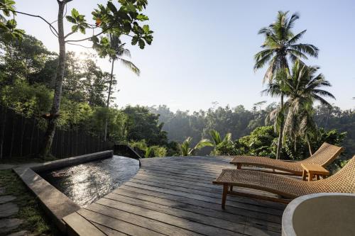 a wooden deck with two chairs and a pool at Bumi Kabins Ubud in Tegalalang