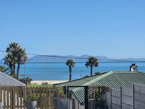 a house with a fence and palm trees and the ocean at Charla on the Beach in Gordonʼs Bay