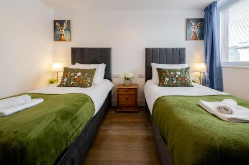 a bedroom with two beds with green sheets and a window at Group-Friendly Flat - 3 Beds, a Sofa Bed & Parking in Andover