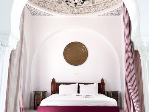 a white bedroom with a bed with a clock on the ceiling at Villa Oasis Hammamet in Hammamet