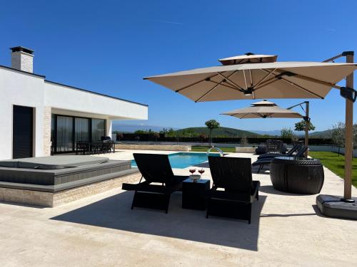 a patio with two chairs and an umbrella and a pool at Villa DEL SOLE with Heated Saltwater Pool, Jacuzzi and Sauna in Ljubuški