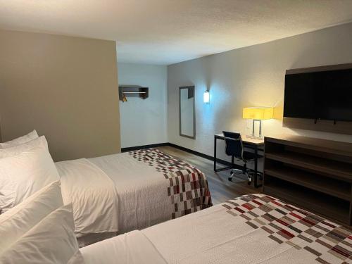 a hotel room with two beds and a desk with a television at Red Roof Inn Kokomo in Kokomo