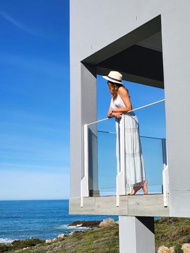 a woman standing on a balcony looking at the ocean at Klipfontein House in Kleinbaai
