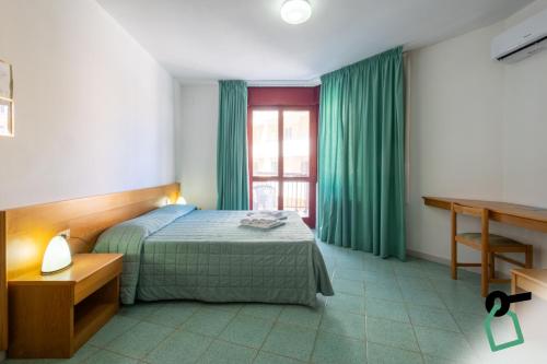 a bedroom with a bed and a window with green curtains at Hotiday Alghero Spiaggia in Alghero