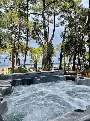 a hot tub with water and trees and a beach at Le Chalet Maguide in Biscarrosse
