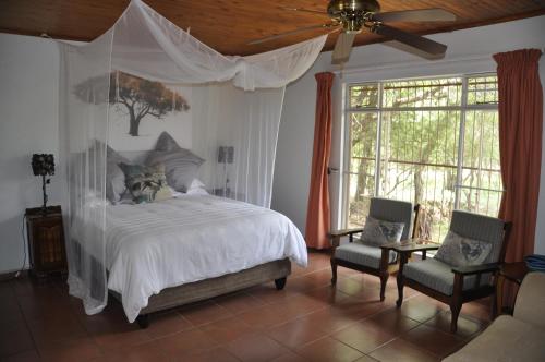 a bedroom with a canopy bed and two chairs at Milkwood Holiday Home in Marloth Park