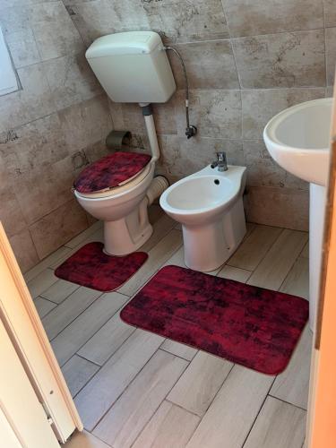 a bathroom with a toilet and a sink and red rugs at Sea View Wooden Houses - Resort Sokoli in Lezhë