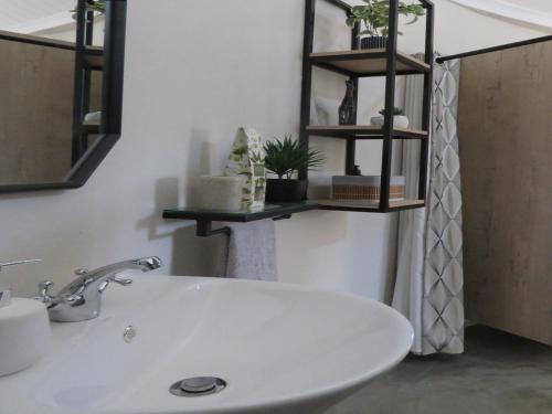 a bathroom with a white sink and shelves on the wall at Pumula Luxury Camps in Lions River