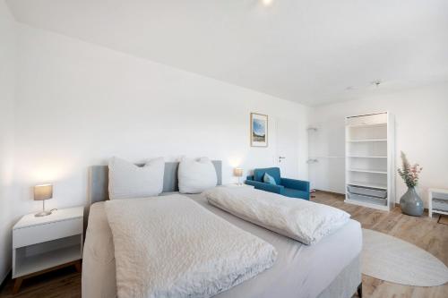 a white bedroom with a large bed and a blue chair at Chalet Seewald - Apartment in Seewald