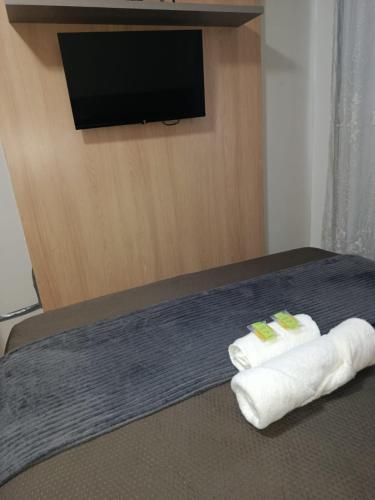 a bedroom with two towels on a bed with a flat screen tv at Apartamento 1 km da praia com ar e garagem in Vila Velha