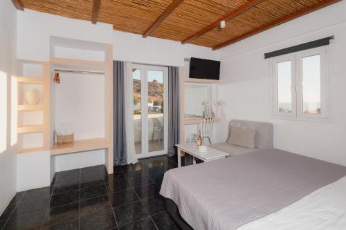 a bedroom with a bed and a chair and windows at Skala Sunset Hotel and spa in Ios Chora