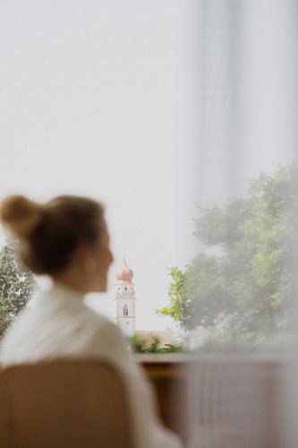 a woman sitting in a chair with a clock tower in the background at SIEGI apartments & retreat - Merano Südtirol in Parcines