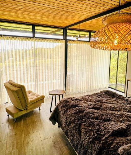 a bedroom with a bed and a chair and windows at Cabaña MonteCristo in El Peñol