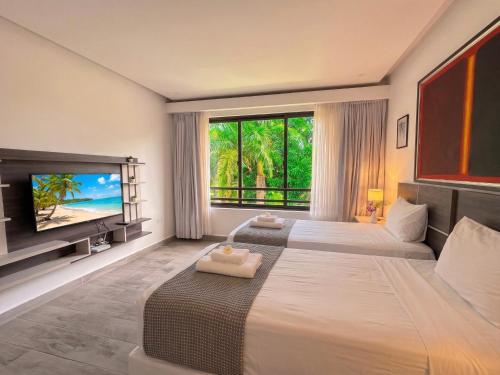 a bedroom with two beds and a tv and a window at Hotel NEON by Playa Palmera Beach Resort in Punta Cana
