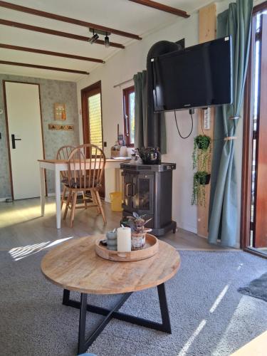 a living room with a table and a flat screen tv at Chalet Vuurvos - sfeervol chalet met omheinde tuin, midden in de bossen van Drenthe in Eext