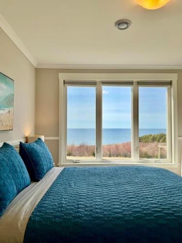 a bedroom with a large bed and two windows at Oceanfront Escape on the Cabot Trail by Cabotopia in Chéticamp