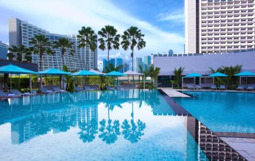 a large swimming pool with blue umbrellas and palm trees at Pan Pacific Singapore in Singapore