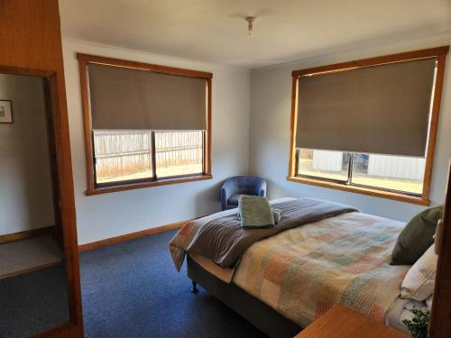 ein Schlafzimmer mit zwei Fenstern, einem Bett und einem Stuhl in der Unterkunft Zeehan Affect in Zeehan