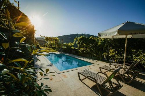a swimming pool with two chairs and an umbrella at Casa da Garrafeira - Quinta da Portela in Terras de Bouro