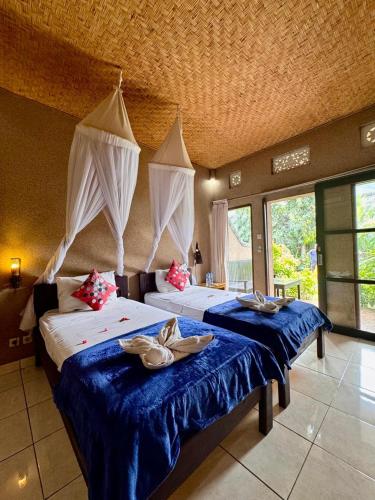 two beds in a room with blue sheets and red pillows at Sudi Guest House in Pemuteran