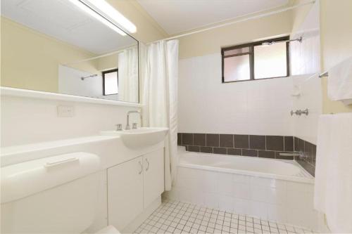 a white bathroom with a sink and a bath tub at Mt Ommaney Hotel Apartments in Brisbane